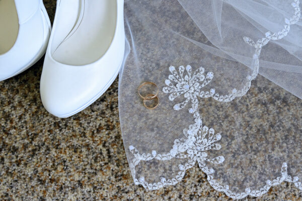 White shoes with heels and gold wedding rings on white lace veil.