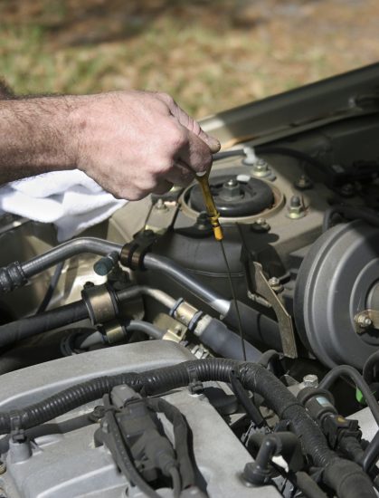 A closeup of a mechanic's hand pulling on the dipstick to check a car's oil. Photo taken as work was actually being performed.