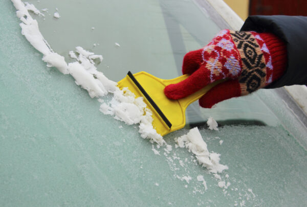 Hand of woman in glove scraping ice and snow from car windscreen